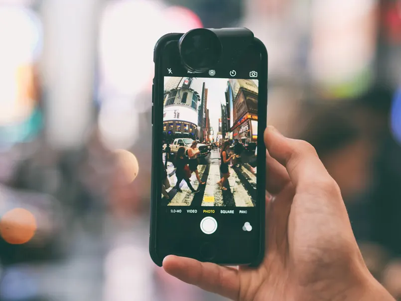 Eine Hand hält ein Smartphone hoch und fotografiert damit eine unscharfe Straßenszene