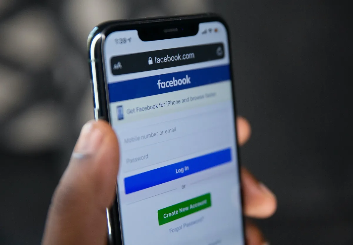 Eine Hand hält ein Smartphone mit der Anmeldeseite von Facebook