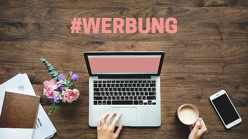 Schreibtisch von oben: Hände tippen auf einem Laptop, dessen Bildschirm in großen Buchstaben „#WERBUNG“ zeigt