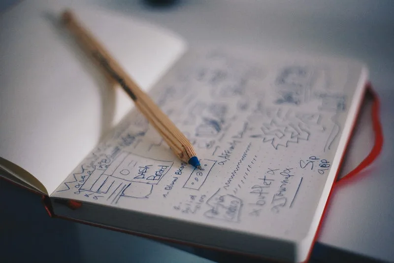 Ein aufgeschlagenes Notizbuch mit handgezeichneter Skizze und einem Bleistift