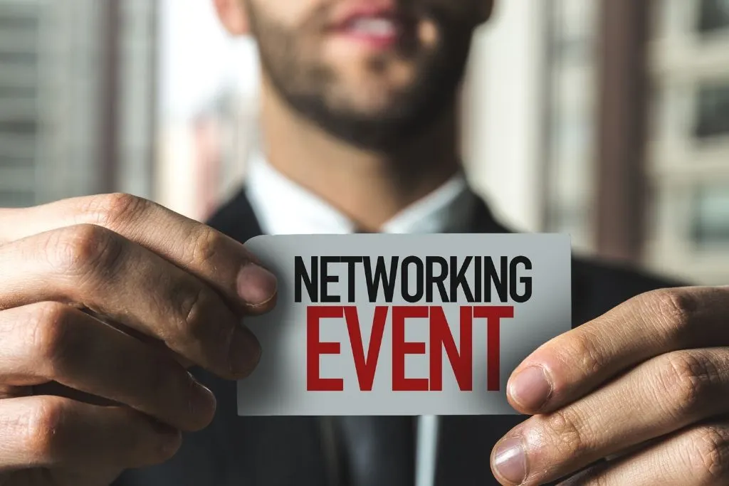 Ein Mann im Anzug hält eine Karte mit der Aufschrift „Networking Event“ in die Kamera